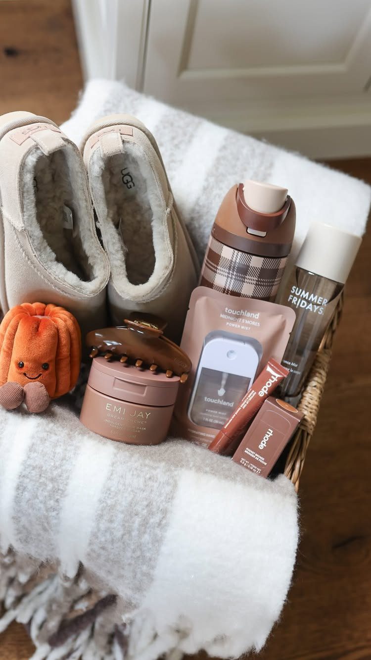 8 Fall Inspired Gifts for Cozy Autumn Gatherings 1 Wicker gift basket containing beige slippers, plush pumpkin, skincare, and a plaid thermos.