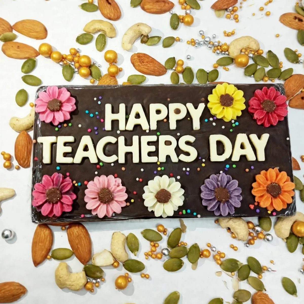 Chocolate bar with Happy Teachers Day lettering and colorful frosting flowers among nuts.