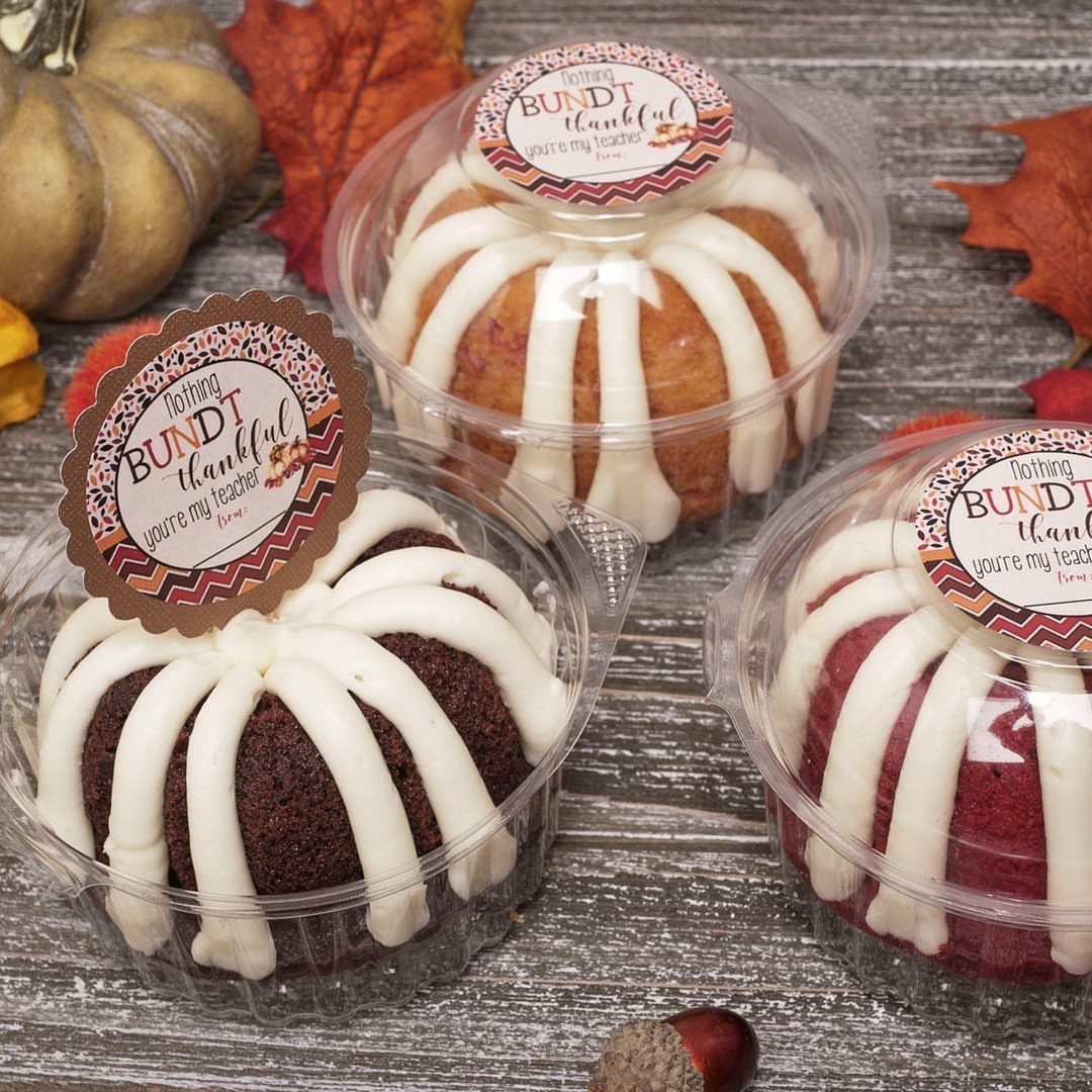 Three mini bundt cakes with icing and teacher thank you tags among autumn leaves.