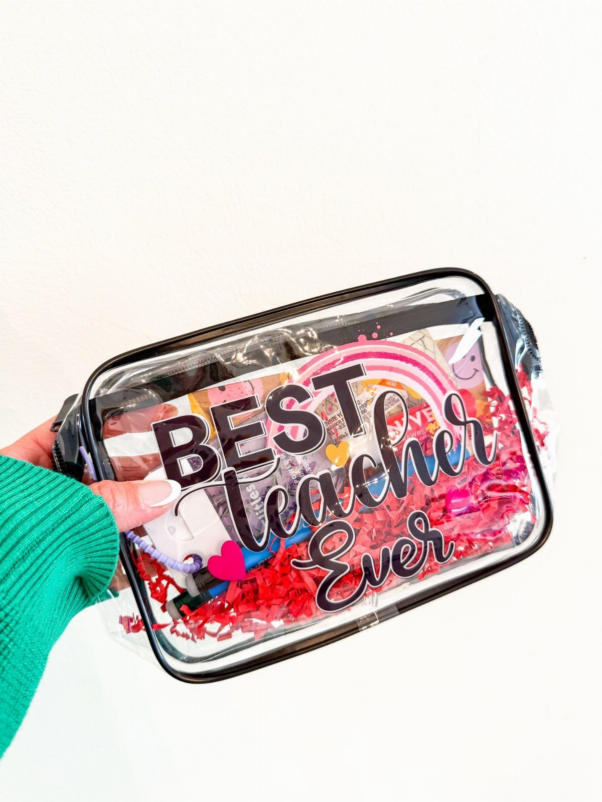 Clear plastic gift pouch filled with red shred and teacher-themed items.