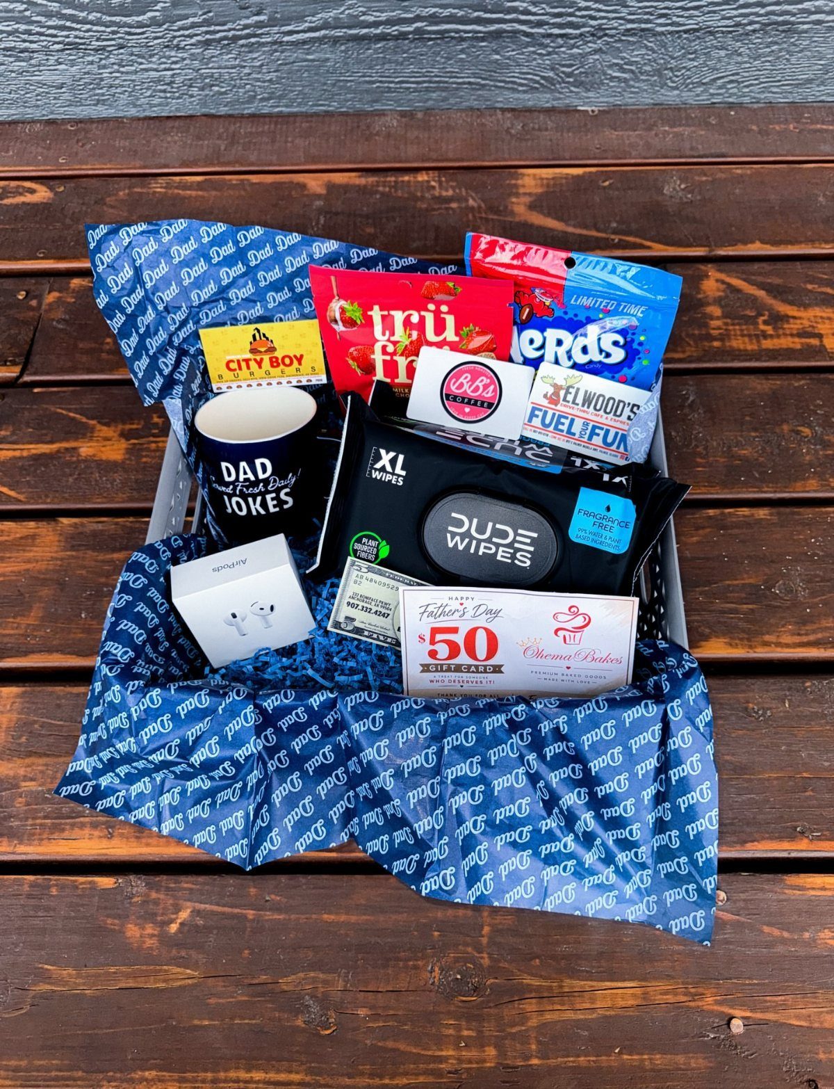 8 Father's Day Gift for Employees Ideas Dads Will Use 4 Father's Day gift basket with snacks, a mug, and a gift card on wood.