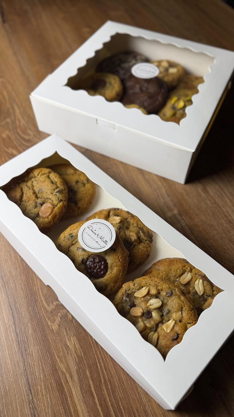 Assorted gourmet cookies in white gift boxes on a wooden table.