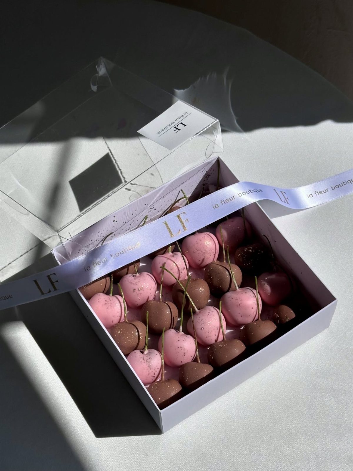 Chocolate-covered cherries in pink and brown coatings arranged in a white gift box.