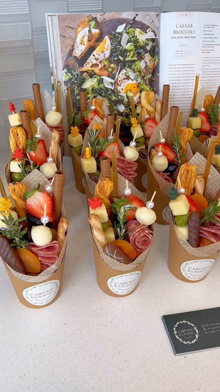Charcuterie cones filled with meats, cheeses, and fruits next to an open cookbook.
