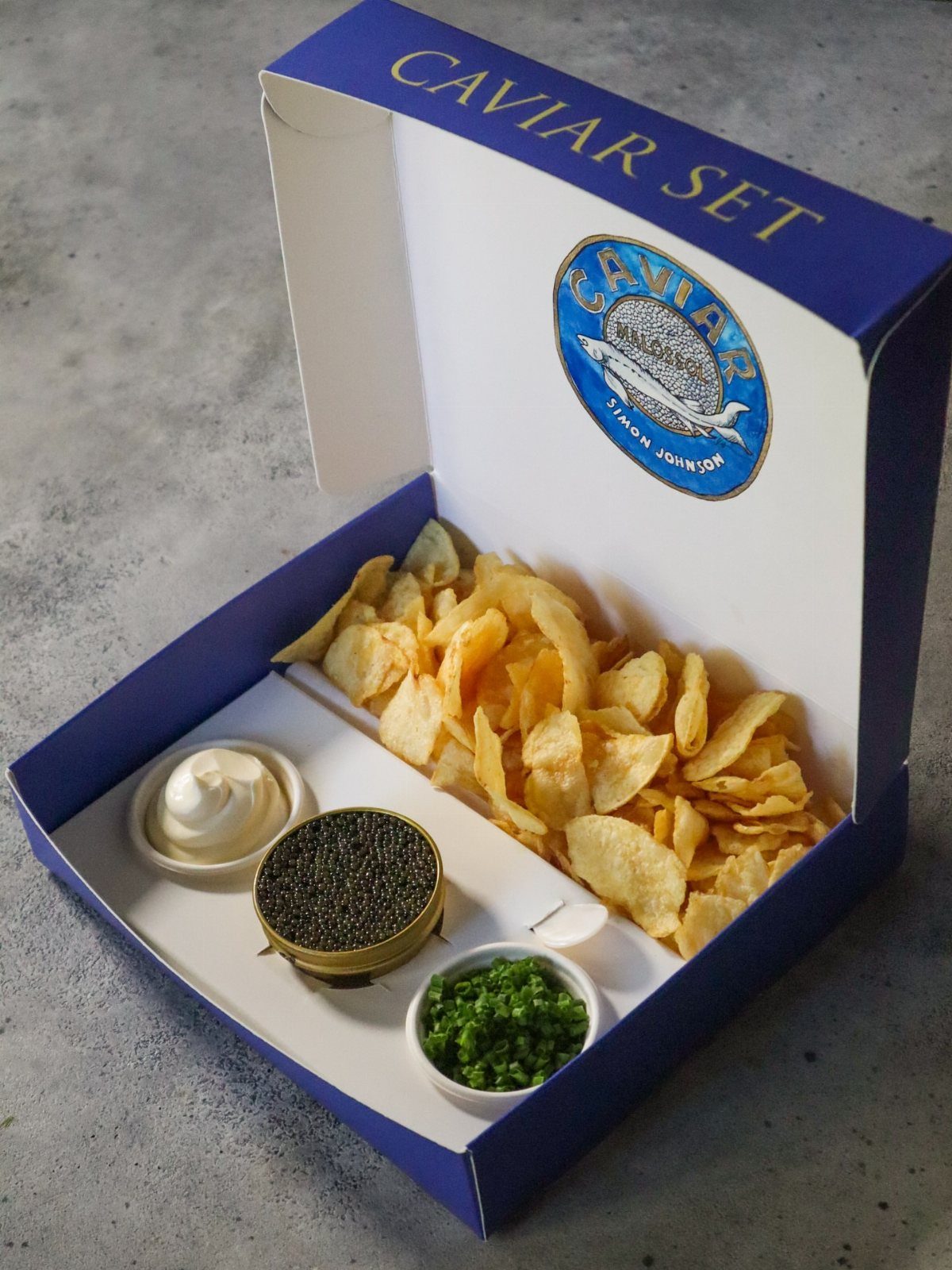Caviar set in a blue box with potato chips, cream, and chives.