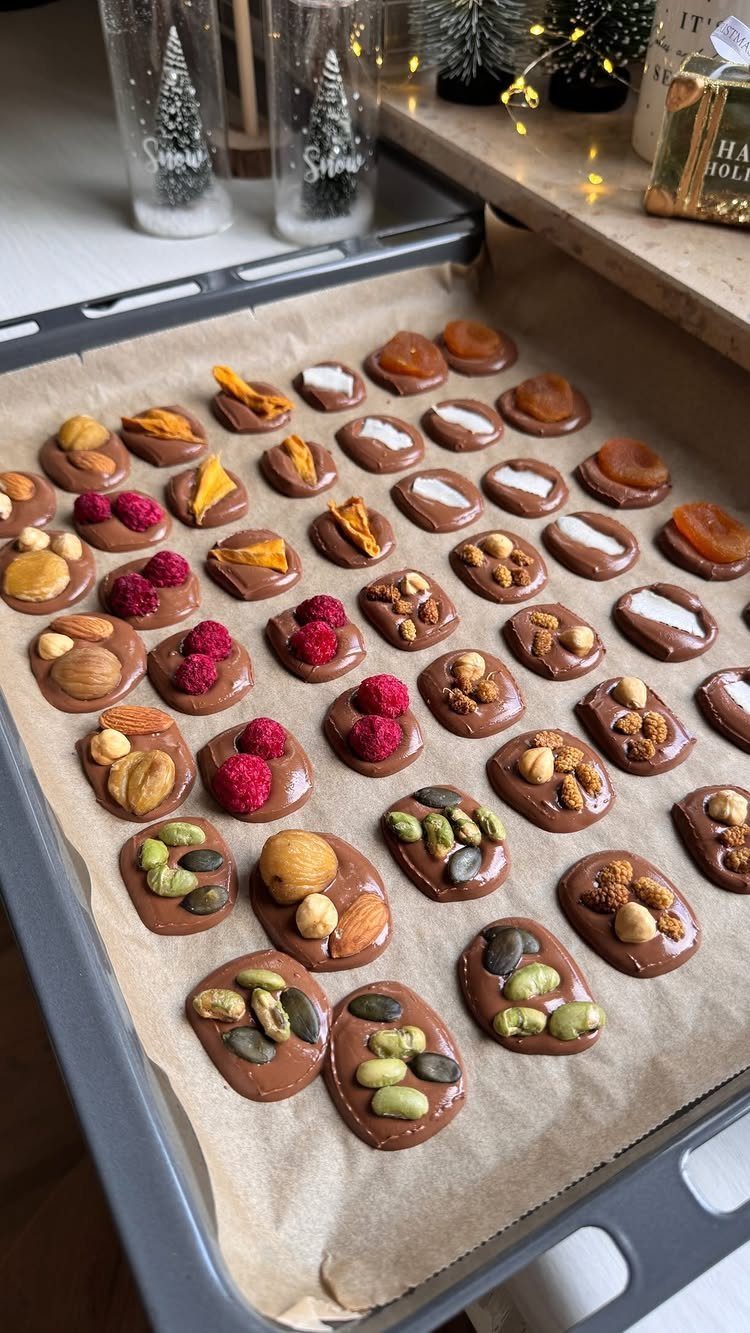 15 Friendsgiving Gift Ideas for Hosts and Guests 8 Chocolate treats topped with nuts and berries on a baking tray with parchment paper.