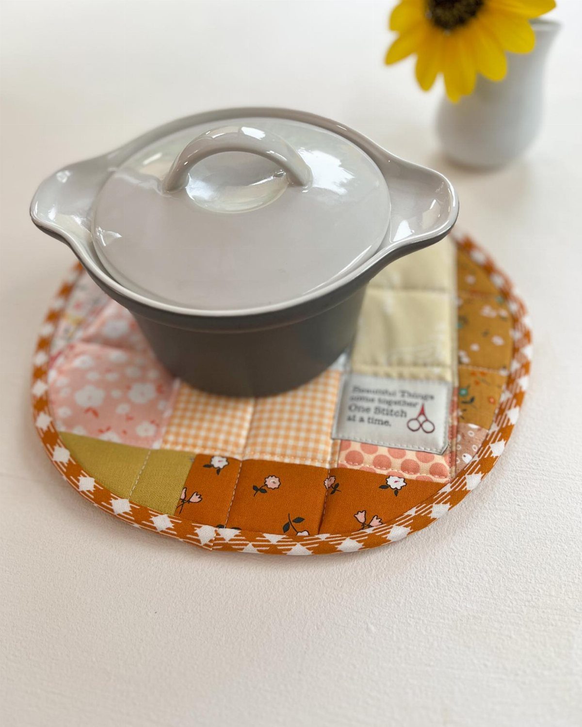 15 Friendsgiving Gift Ideas for Hosts and Guests 13 Grey ceramic pot on a colorful quilted fabric trivet with autumn tones.