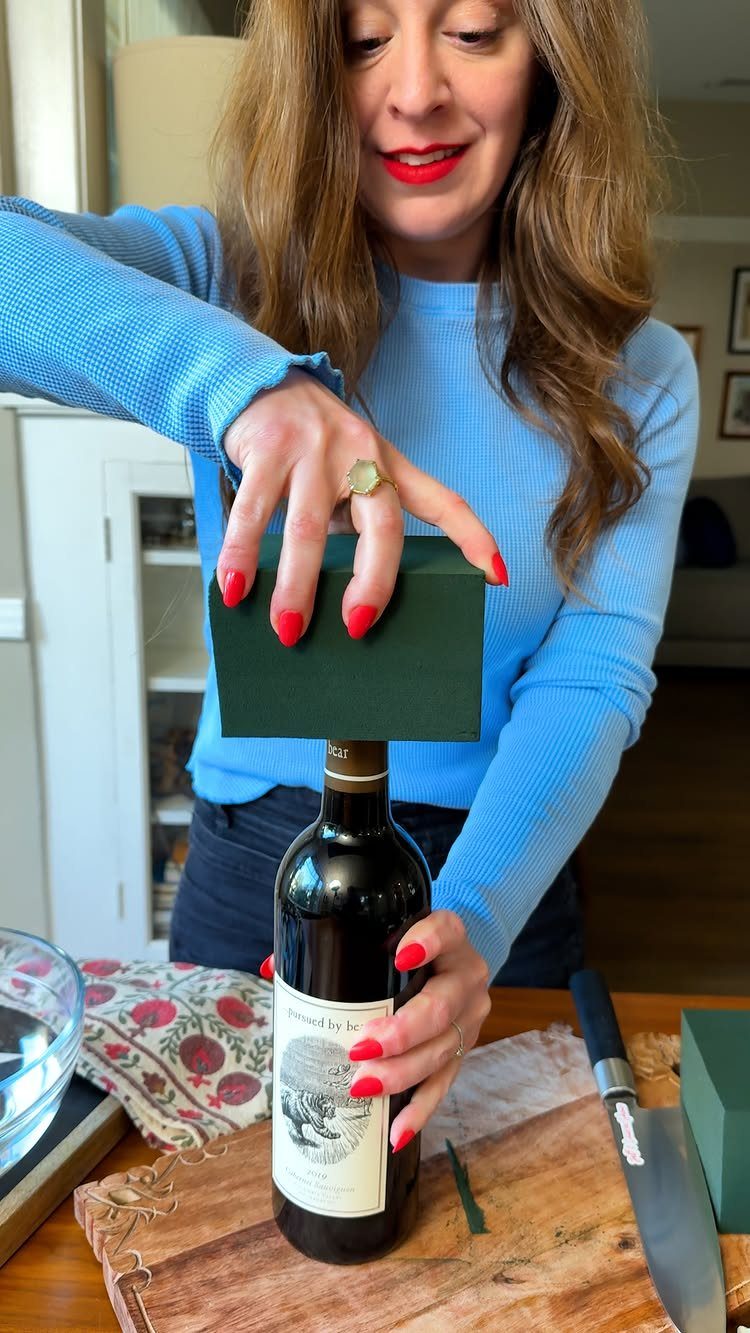 15 Friendsgiving Gift Ideas for Hosts and Guests 14 Woman placing a green gift box on top of a wine bottle gift.