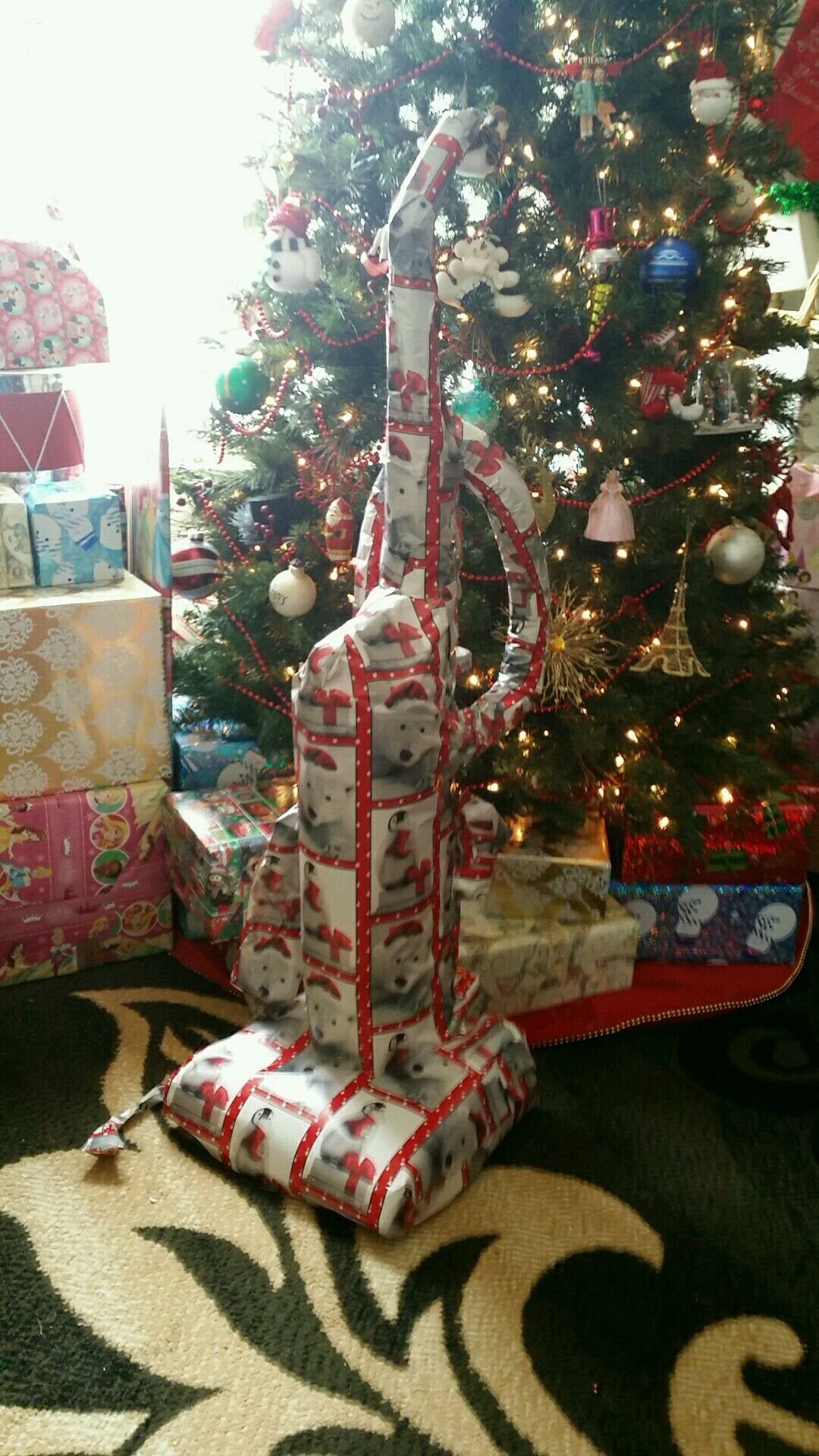 9 Funny Christmas Gift Wrapping Ideas Your Family Will Love 3 Wrapped plunger standing upright in front of a decorated Christmas tree and gifts.