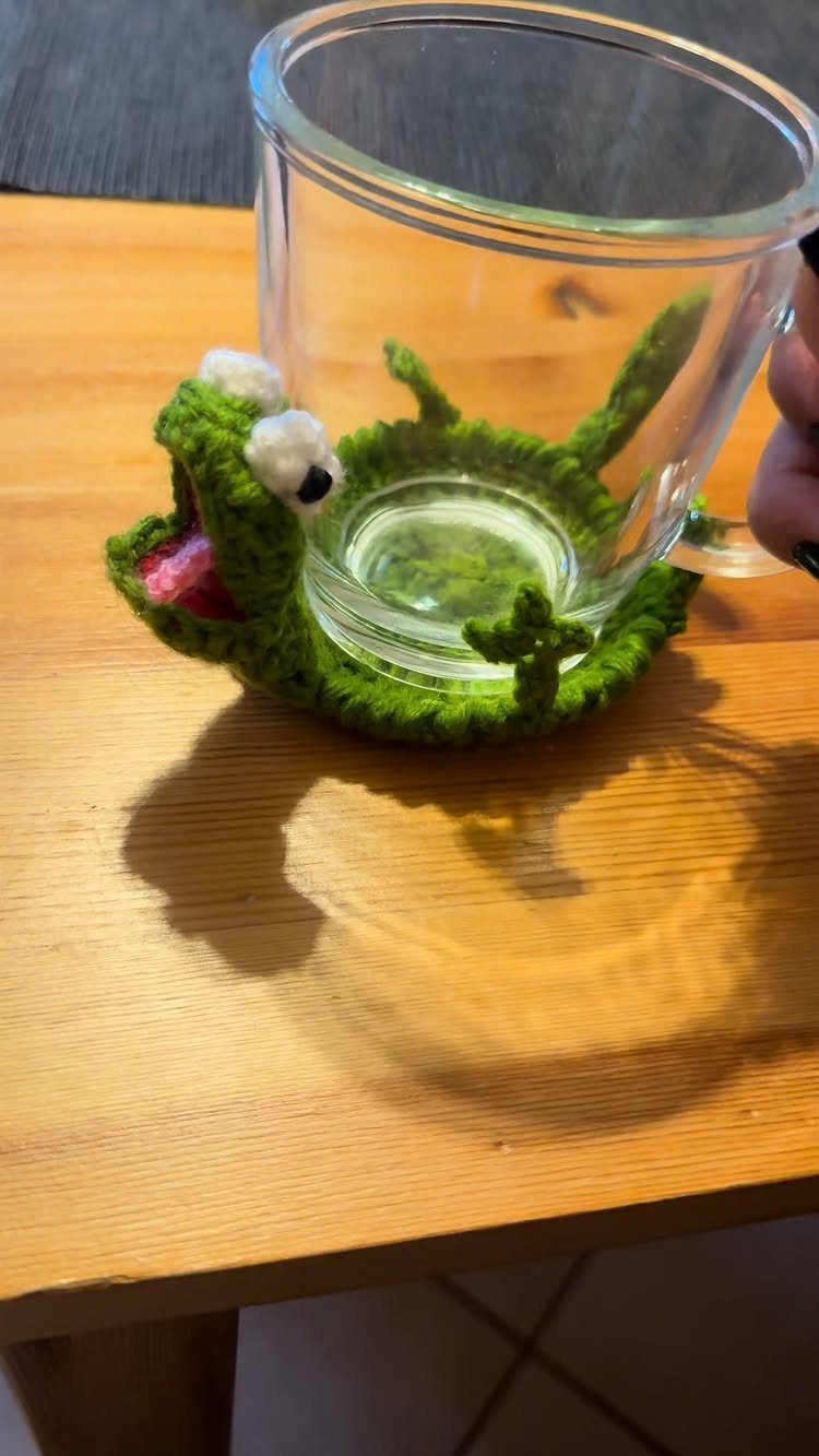 13 Funny Gag Gift Ideas for Birthdays and Office Parties 5 Clear glass cup resting on a green crocheted frog-shaped coaster on wooden table