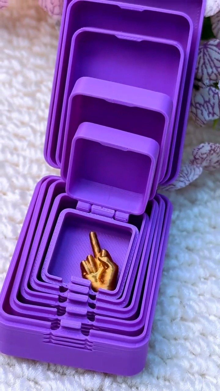 13 Funny Gag Gift Ideas for Birthdays and Office Parties 9 Nested purple boxes opening to reveal a small gold middle finger hand figurine.