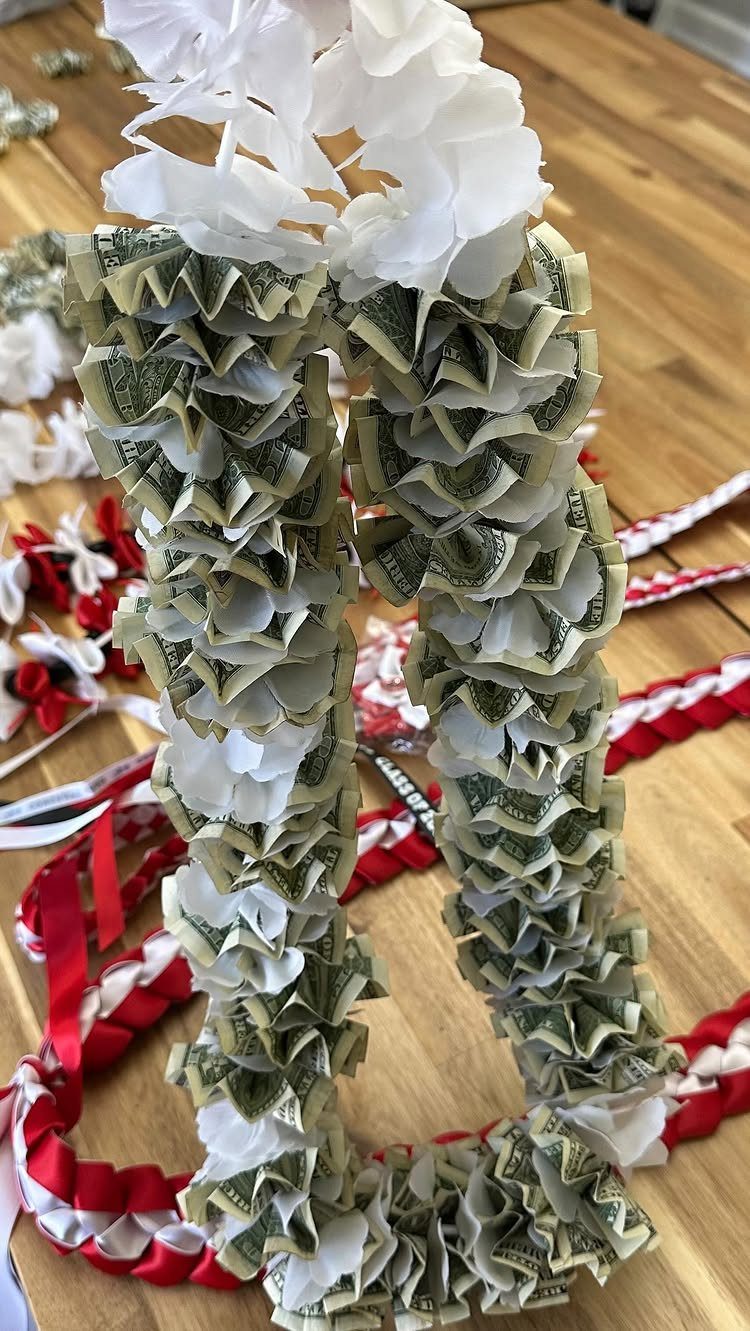 9 Funny Money Gift Ideas to Make Cash Feel Like a Gift 2 Money lei made from folded dollar bills and white paper flowers on wood
