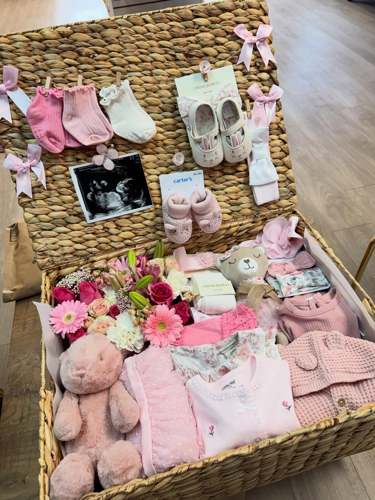 5 Gender Reveal Gifts for Parents-to-Be and Baby 3 Woven wicker keepsake box filled with pink baby clothes, toys, and flowers.