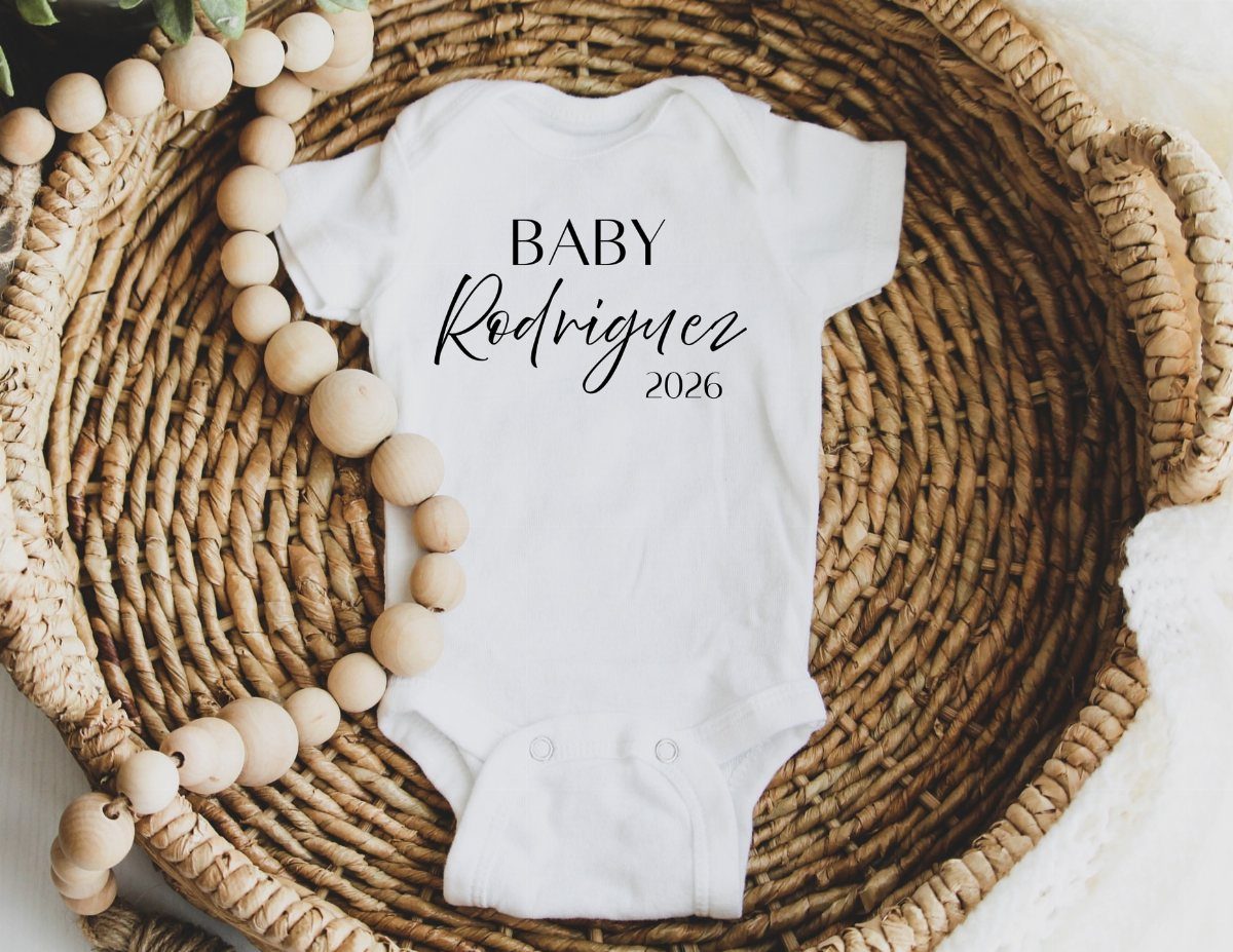 5 Gender Reveal Gifts for Parents-to-Be and Baby 4 White baby bodysuit with personalized text resting in a woven wicker basket.