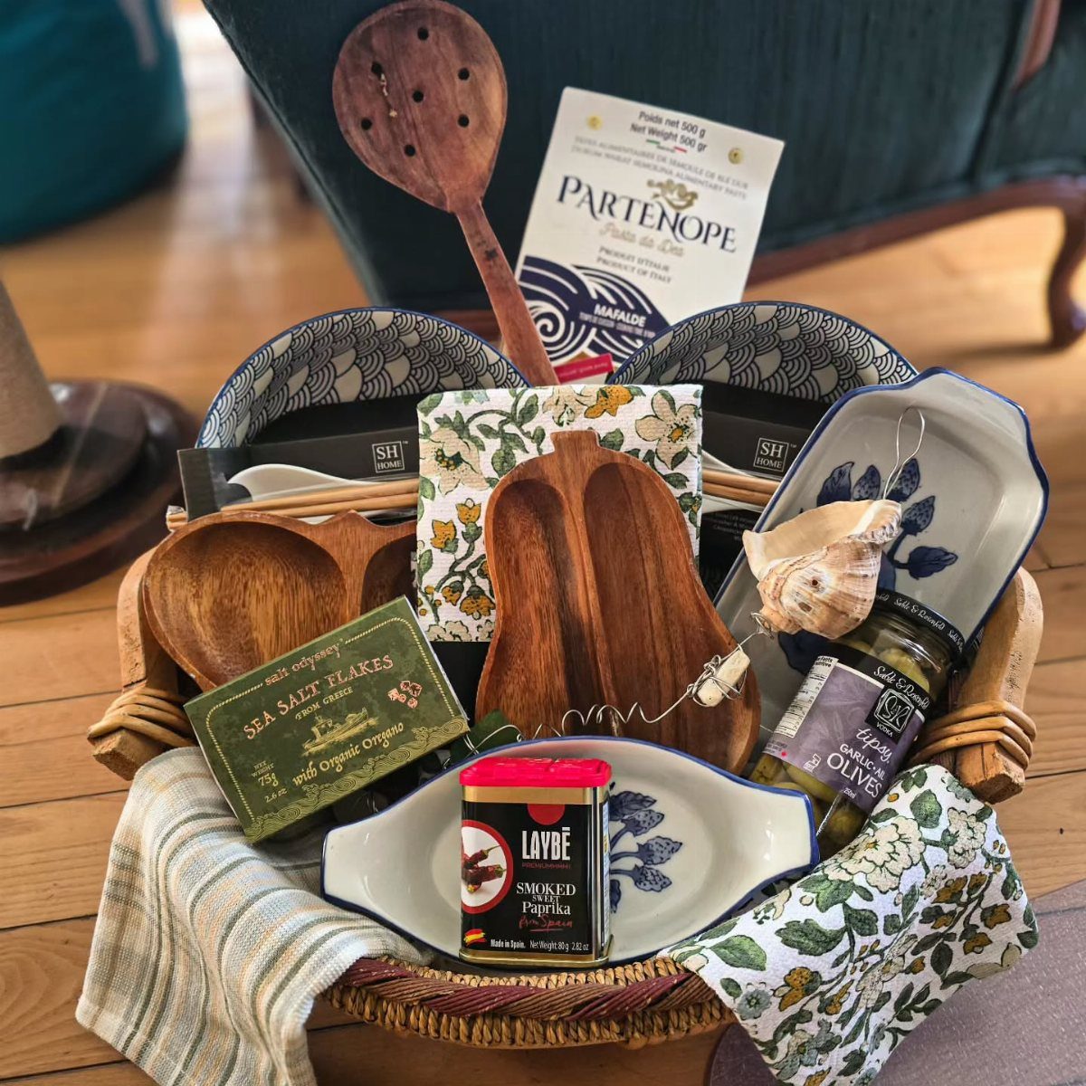 Gift Basket Design: 18 Ideas for Every Occasion 15 Wicker gift basket containing wooden utensils, gourmet spices, olives, and patterned ceramic dishes.