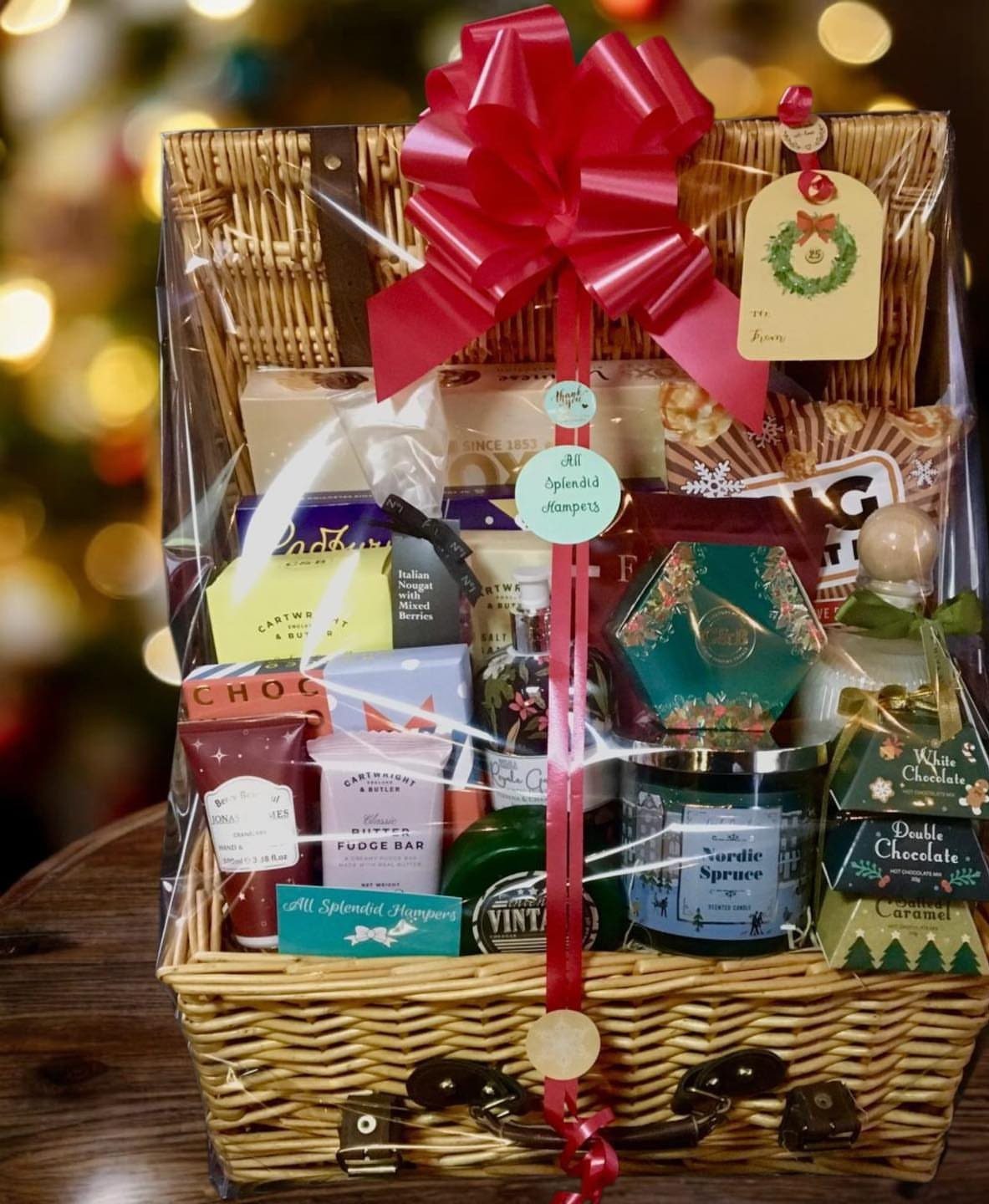 Gift Basket Design: 18 Ideas for Every Occasion 3 Wicker gift basket with gourmet treats and red bow before a Christmas tree.