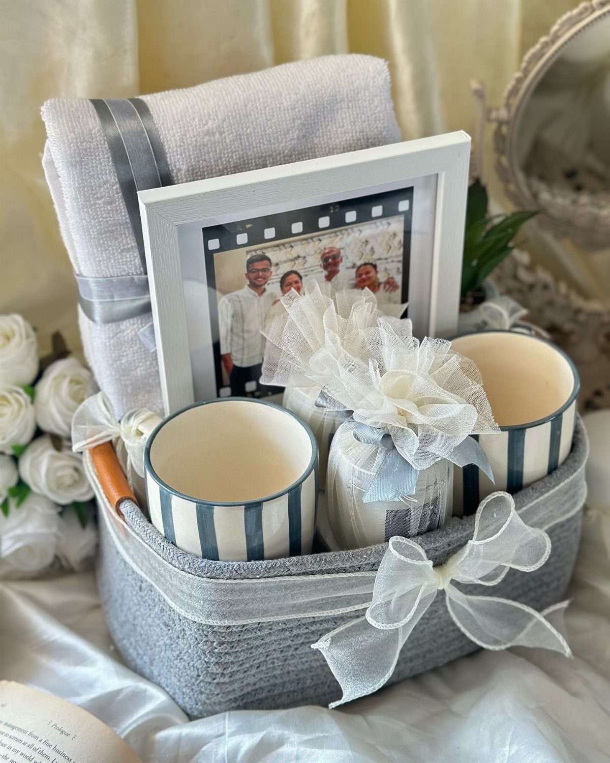 Gift Basket Design: 18 Ideas for Every Occasion 11 Grey fabric gift basket with striped mugs, framed family photo, and folded towel.