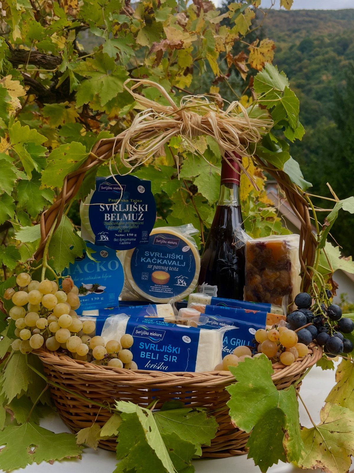Gift Basket Design: 18 Ideas for Every Occasion 5 Wicker gift basket containing wine, assorted cheeses, and fresh grapes among grapevines.