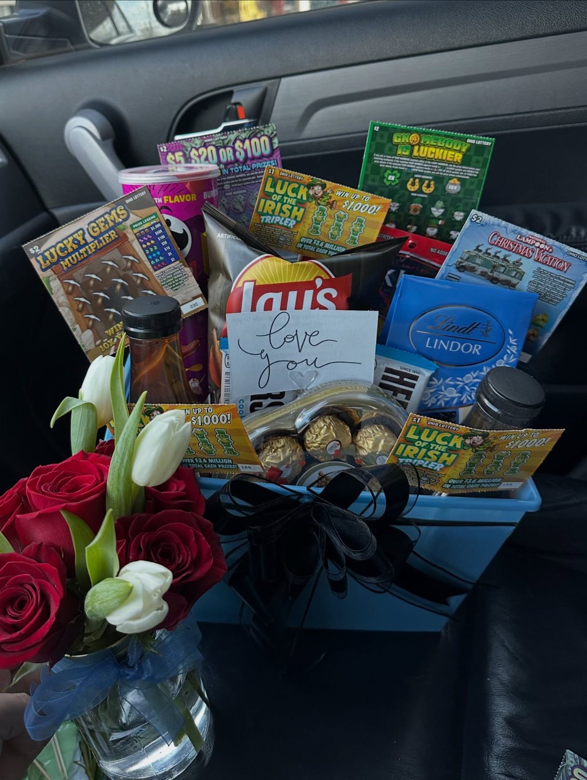 Gift Basket for Couple Ideas: 5 Picks to Give Together 5 Blue gift basket with snacks, chocolates, and lottery tickets next to red roses.