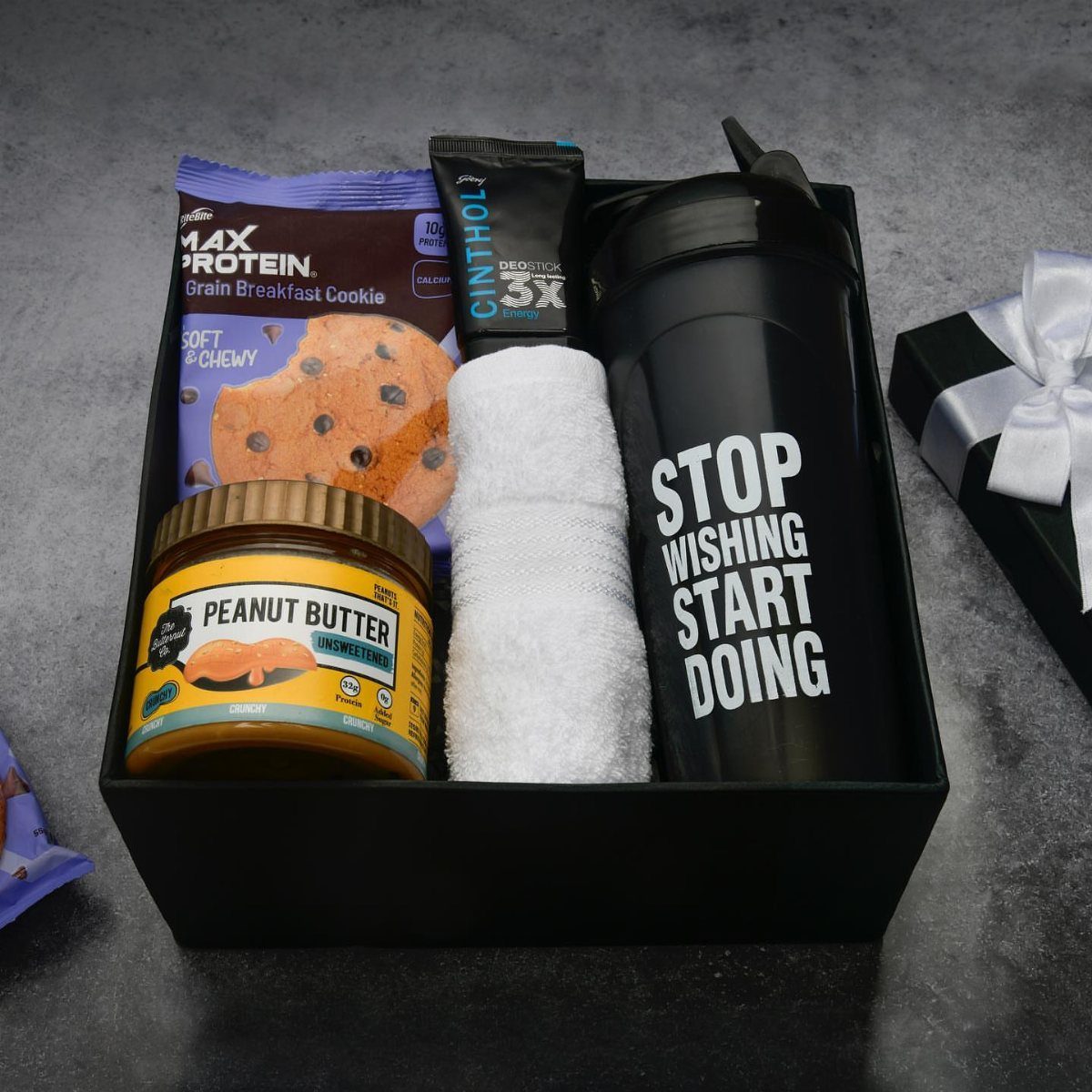 Fitness gift basket with protein cookie, peanut butter, white towel, and black water bottle.