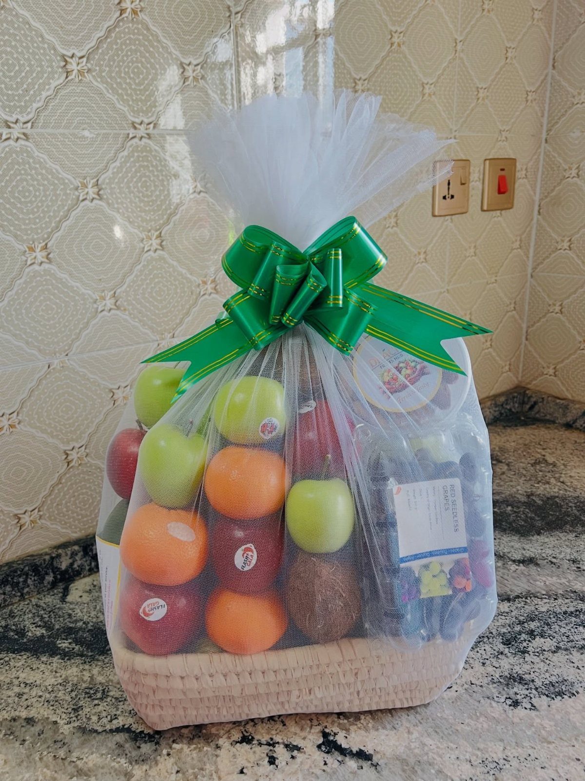 Fruit basket with apples and oranges wrapped in tulle with a green bow