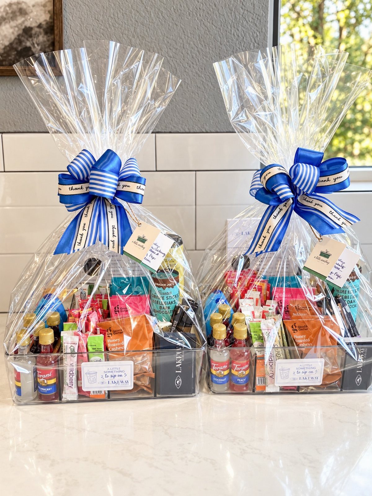 Two wrapped gift baskets with blue bows containing assorted gourmet snacks and treats.