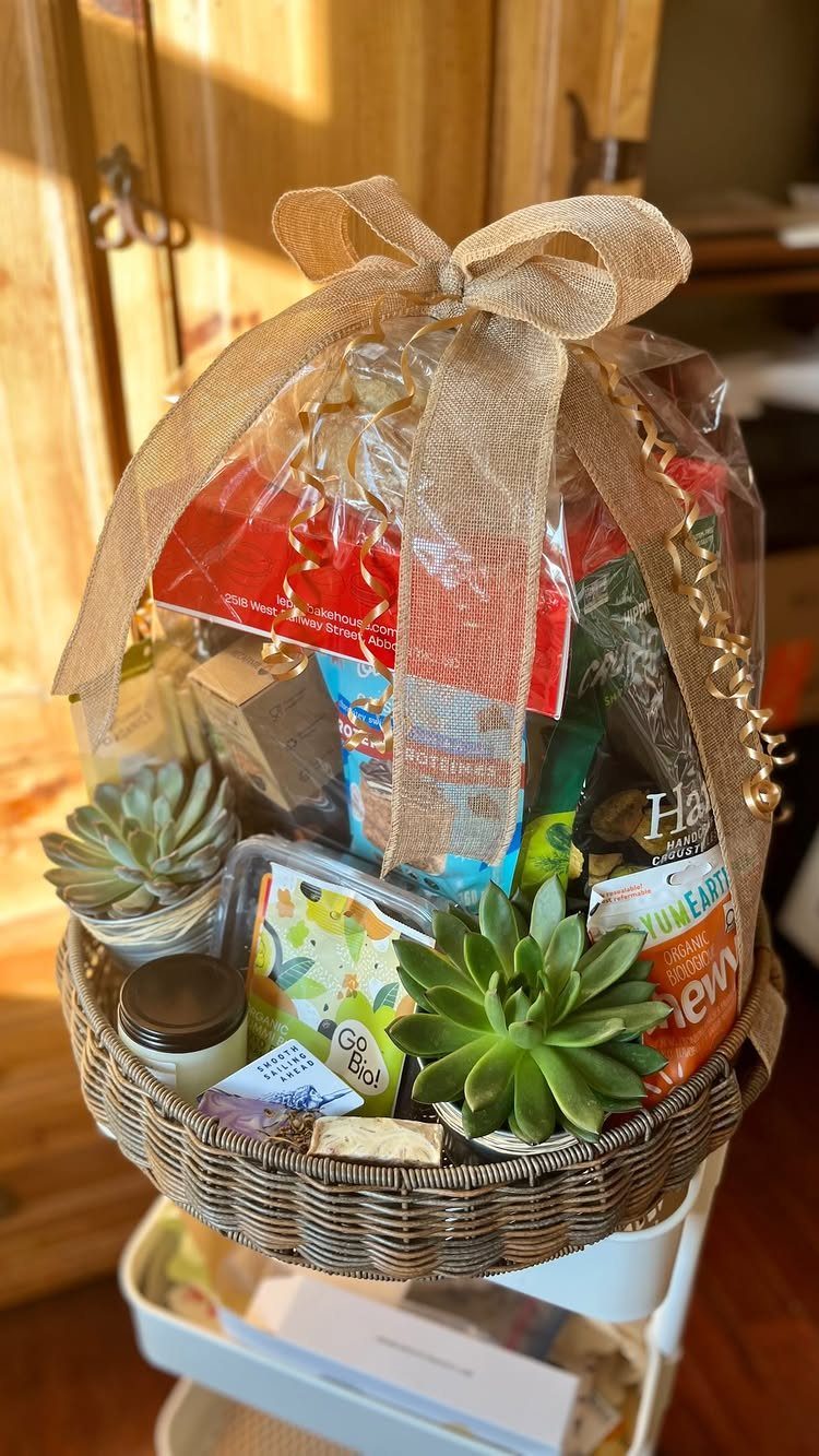 Wicker gift basket with succulents, snacks, and a candle wrapped in cellophane.