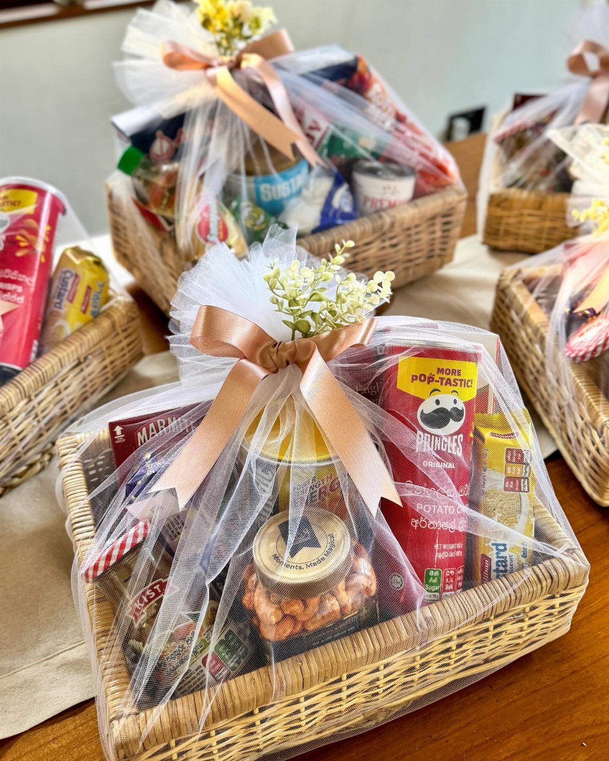 Woven gift baskets filled with snacks and jars wrapped in white tulle ribbons.