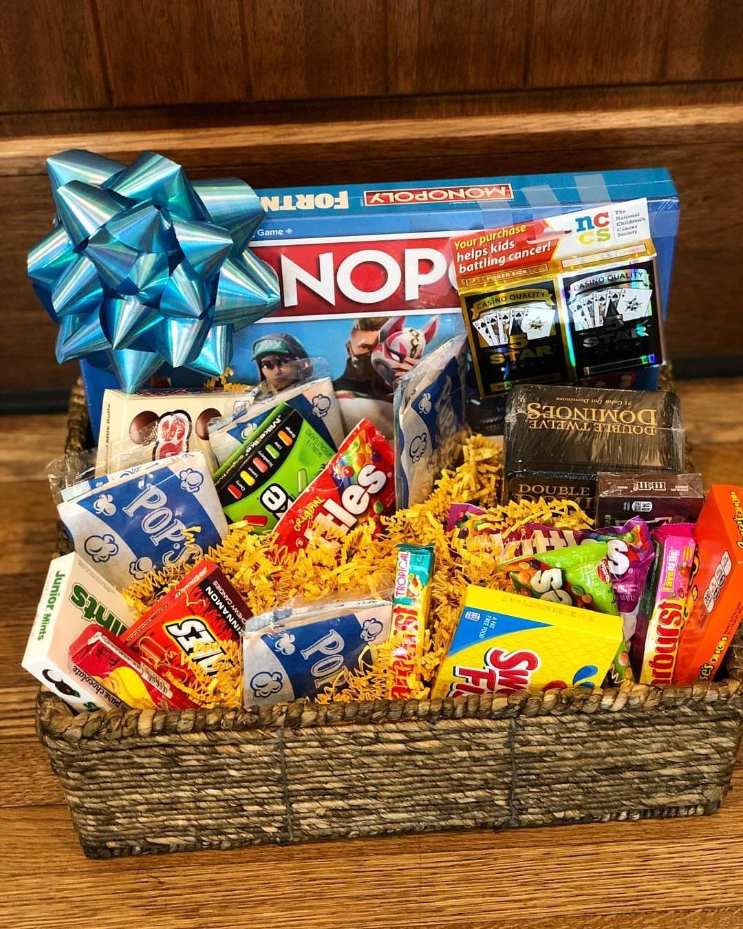 18 Gift Basket Prize Ideas for Raffles and Auctions 16 Woven gift basket filled with board games, snacks, and a large blue bow.