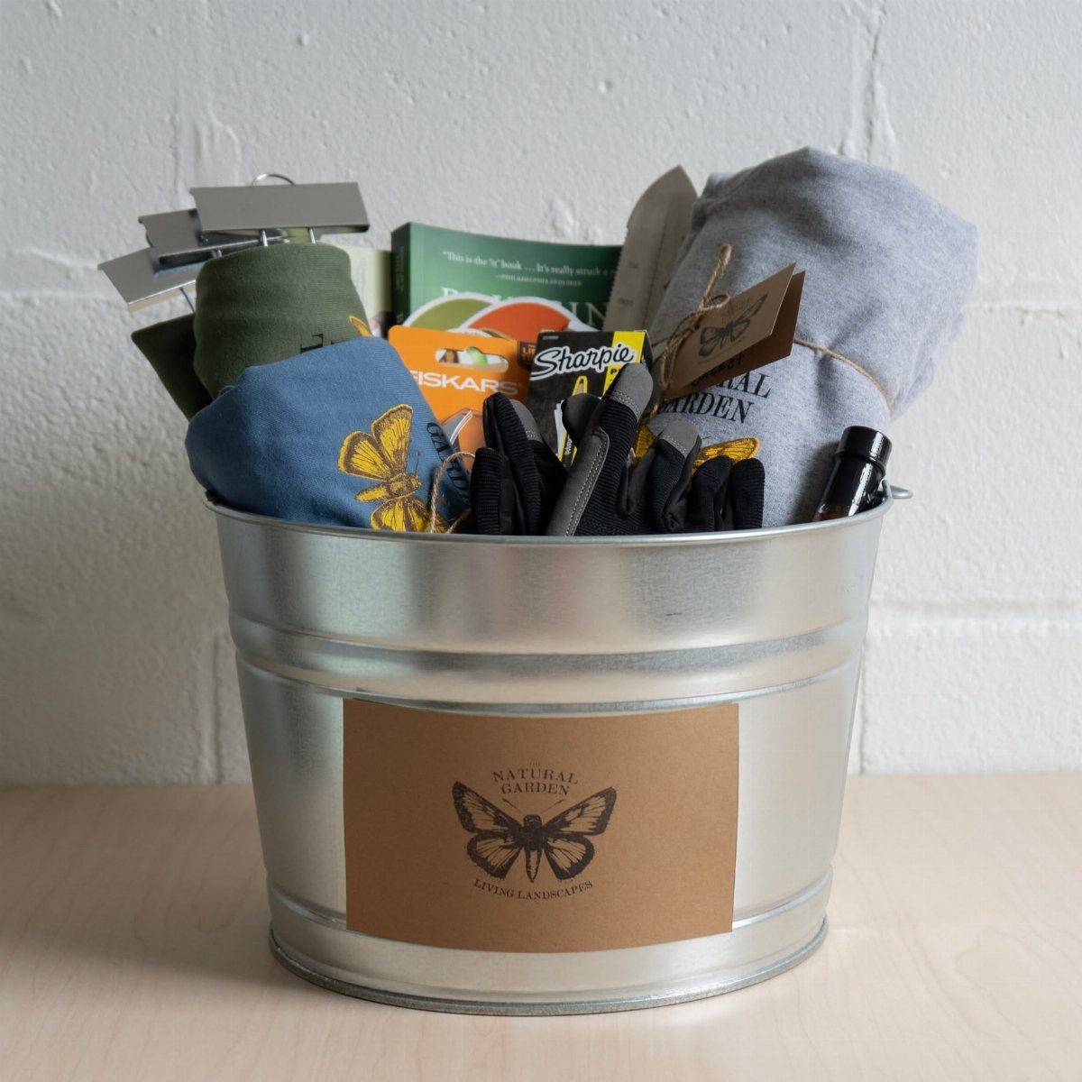 18 Gift Basket Prize Ideas for Raffles and Auctions 9 Galvanized metal bucket filled with gardening gloves, tools, and a butterfly-themed cloth.