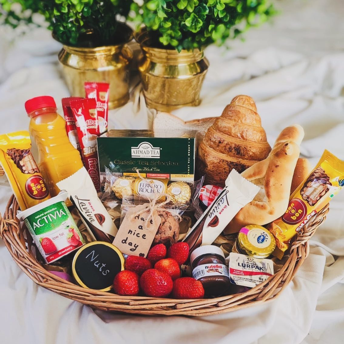 18 Gift Basket Prize Ideas for Raffles and Auctions 18 Wicker gift basket filled with croissants, fruit, juice, and breakfast spreads on white cloth.