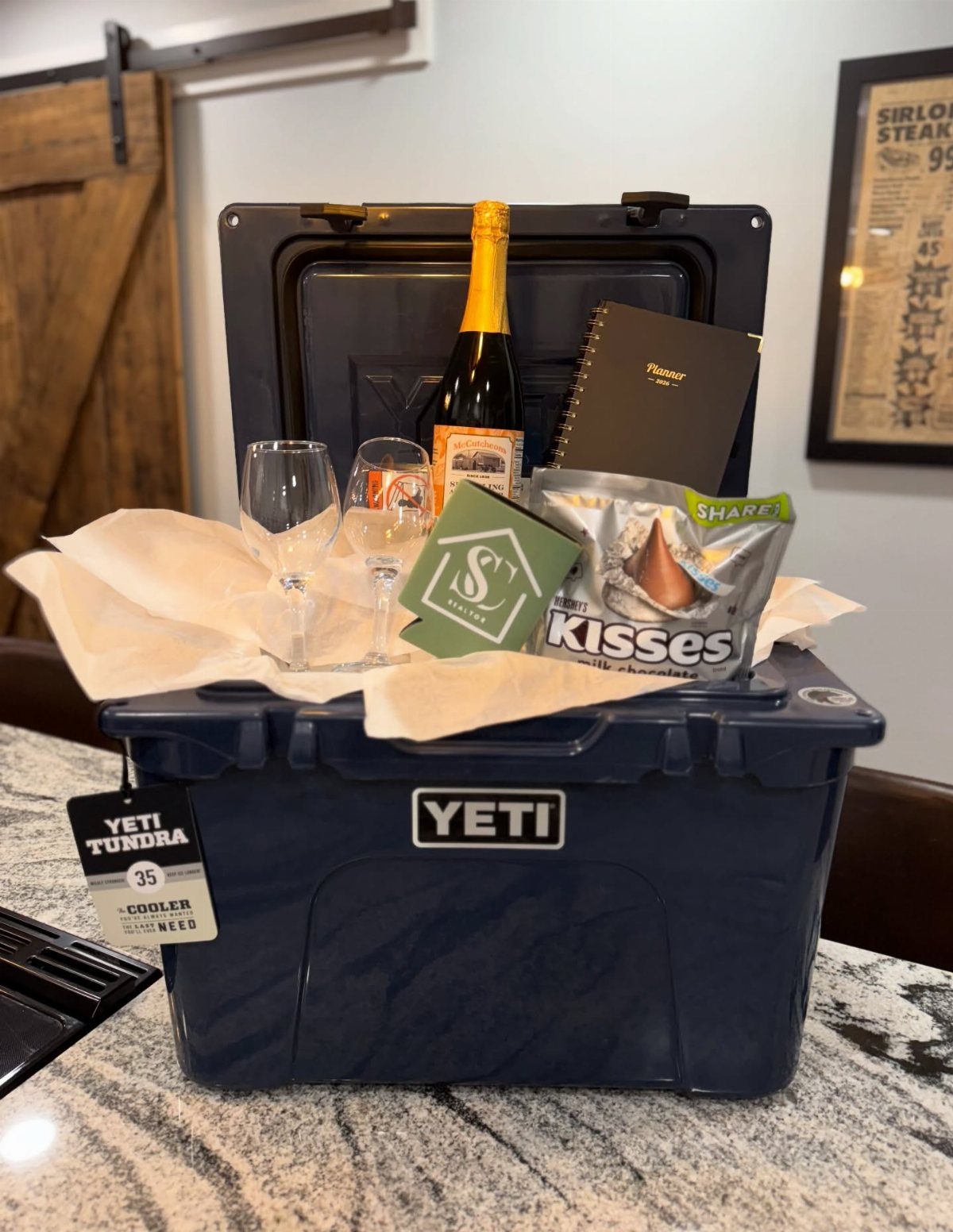 18 Gift Basket Prize Ideas for Raffles and Auctions 14 Navy blue Yeti cooler gift basket with champagne, glasses, and chocolate on granite.