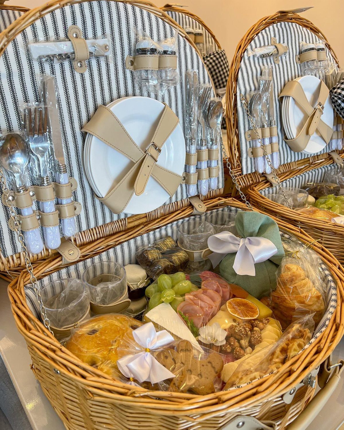 18 Gift Basket Prize Ideas for Raffles and Auctions 11 Wicker picnic baskets filled with gourmet food, white plates, and cutlery for outdoor dining.