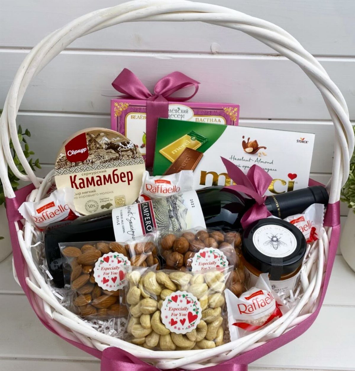 18 Gift Basket Prize Ideas for Raffles and Auctions 2 White wicker gift basket with red wine, cheese, nuts, and chocolates with pink ribbons.