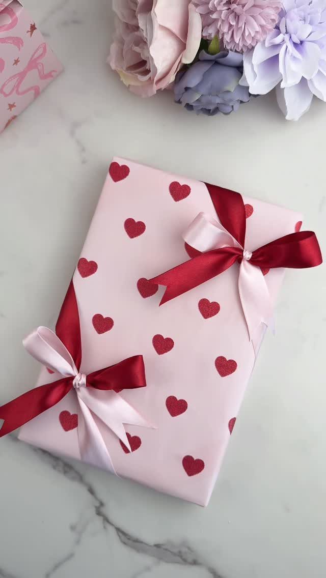 Pink heart-patterned gift box tied with two diagonal red and pink ribbons.