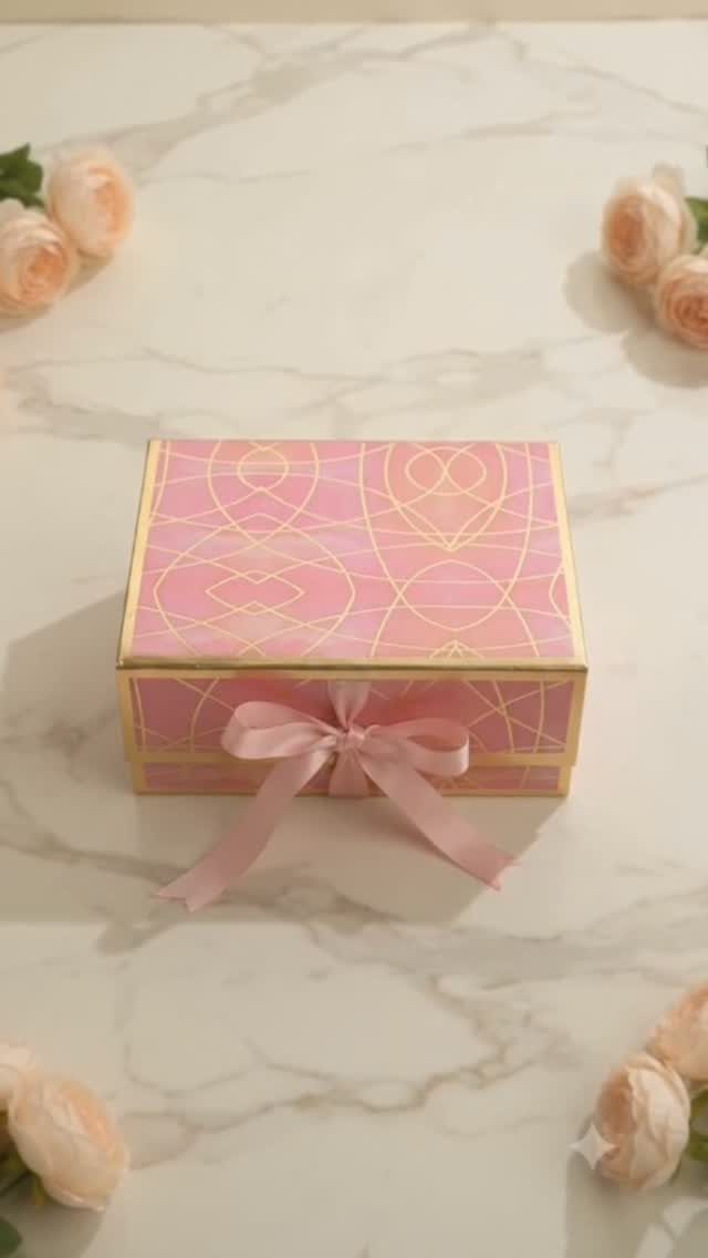Pink patterned gift box with a horizontal pink satin bow on marble surface