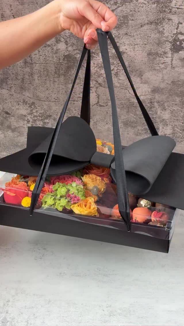 Black luxury gift box with a large bow containing colorful macarons and sweets.