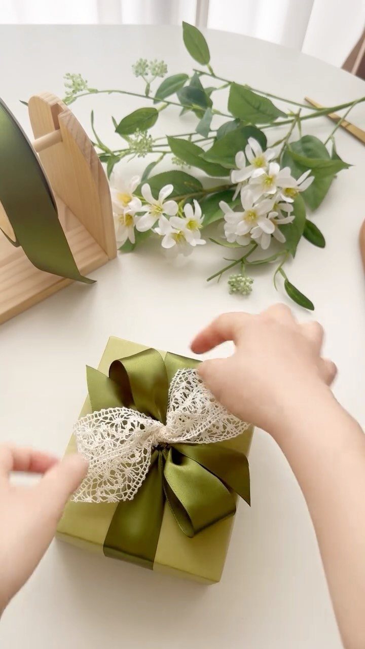 Hands tying a green satin and white lace bow on a green gift box.
