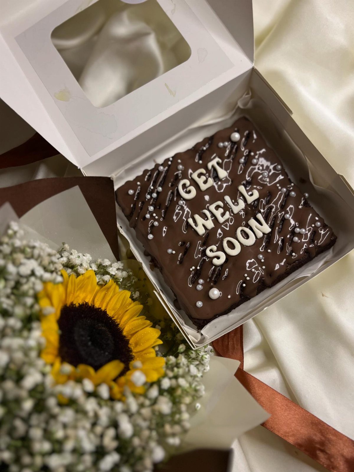 Chocolate brownie with Get Well Soon icing in a box with sunflowers.
