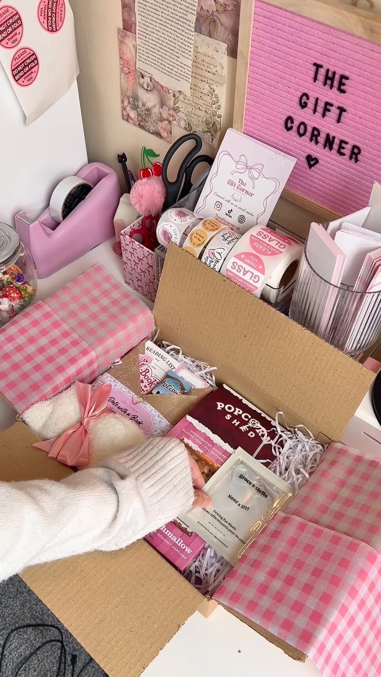 Cardboard gift box containing a book, candle, and pink ribbons on a desk.