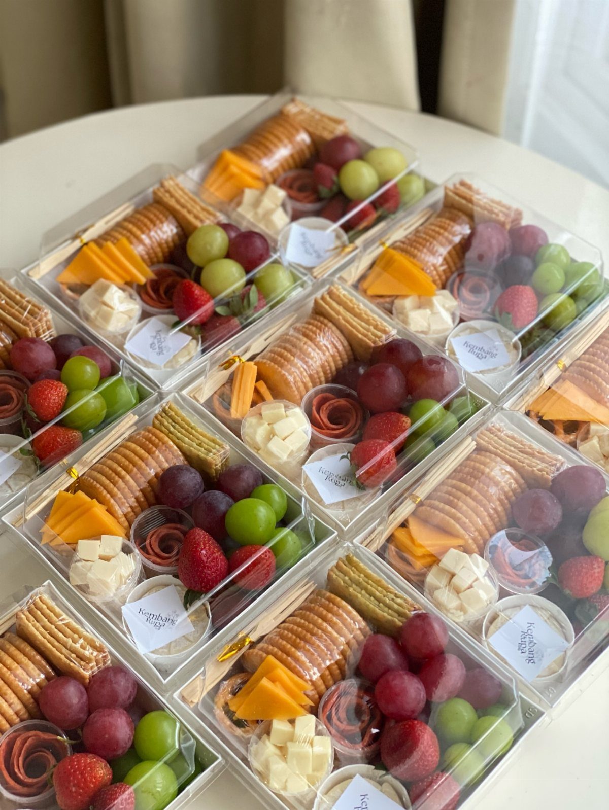 Gourmet cheese and savory snack boxes with salami, grapes, and strawberries.