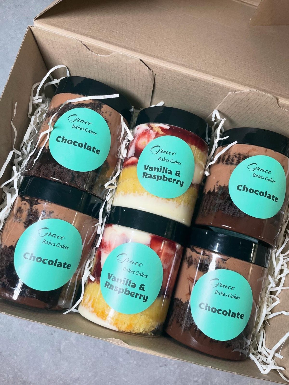 Six dessert jars with chocolate and raspberry layers in a cardboard gift box.