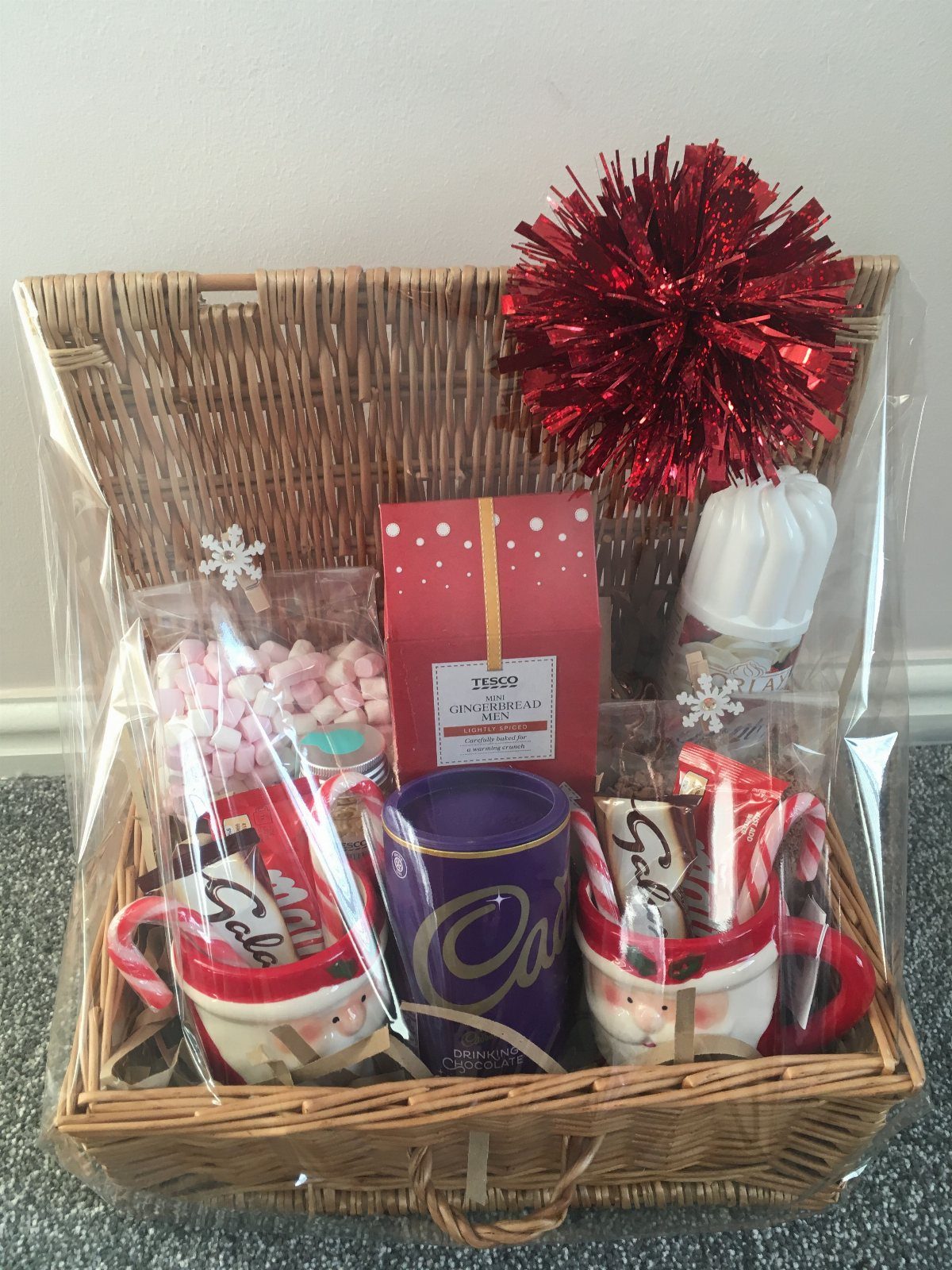 Festive gift basket with cocoa mugs, pink marshmallows, and red holiday decorations.