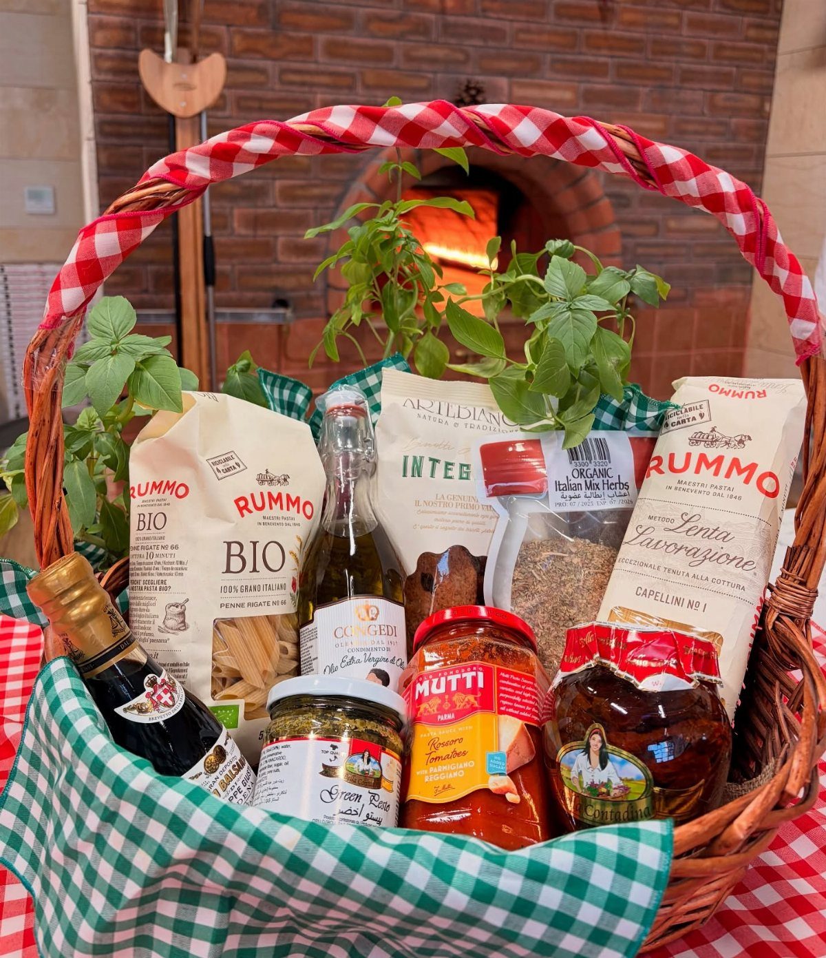 Wicker gift basket filled with Italian pasta, sauces, and oil with fresh basil.