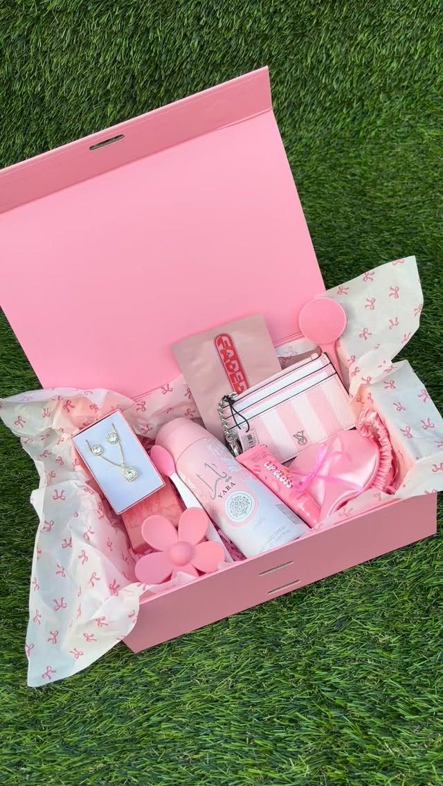 Pink gift hamper containing a necklace, skincare products, and accessories on green grass.