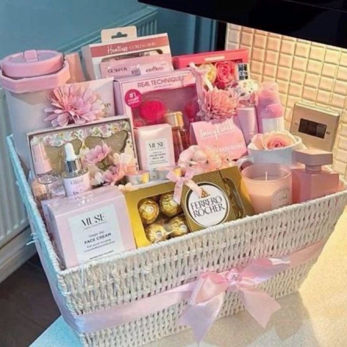 White wicker gift basket filled with pink beauty products, flowers, and chocolates.