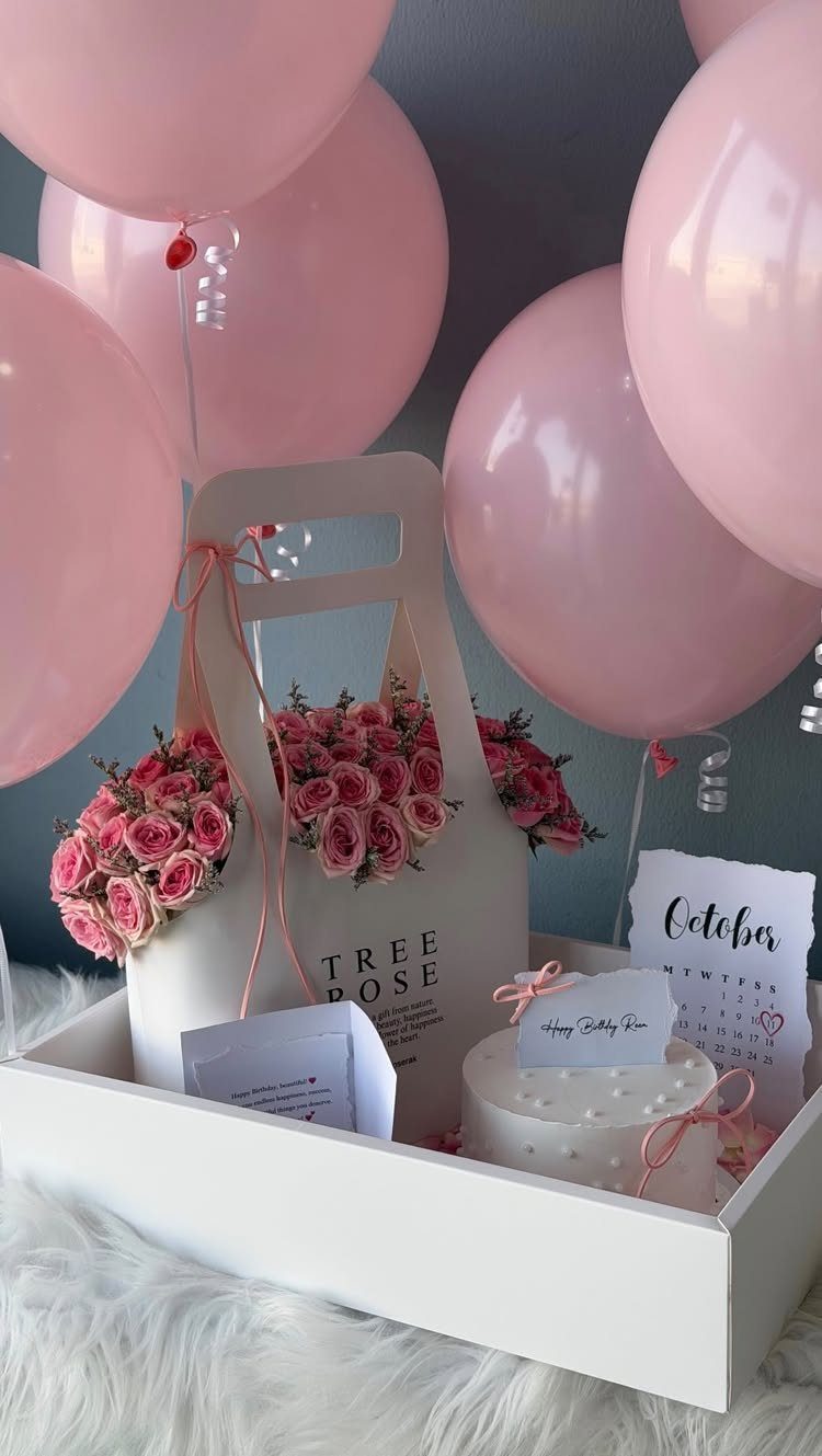 White gift tray with pink roses, a small cake, and pink balloons.