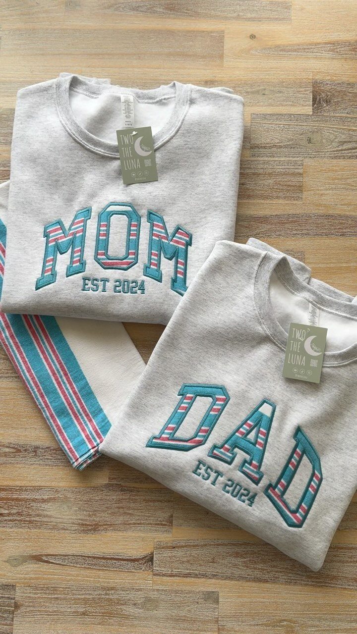 Two grey sweatshirts with MOM and DAD printed in blue and red stripes.