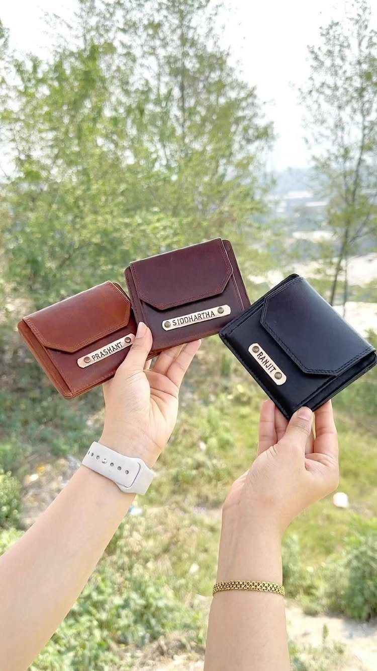 Three small leather wallets in brown, dark brown, and black with gold nameplates.