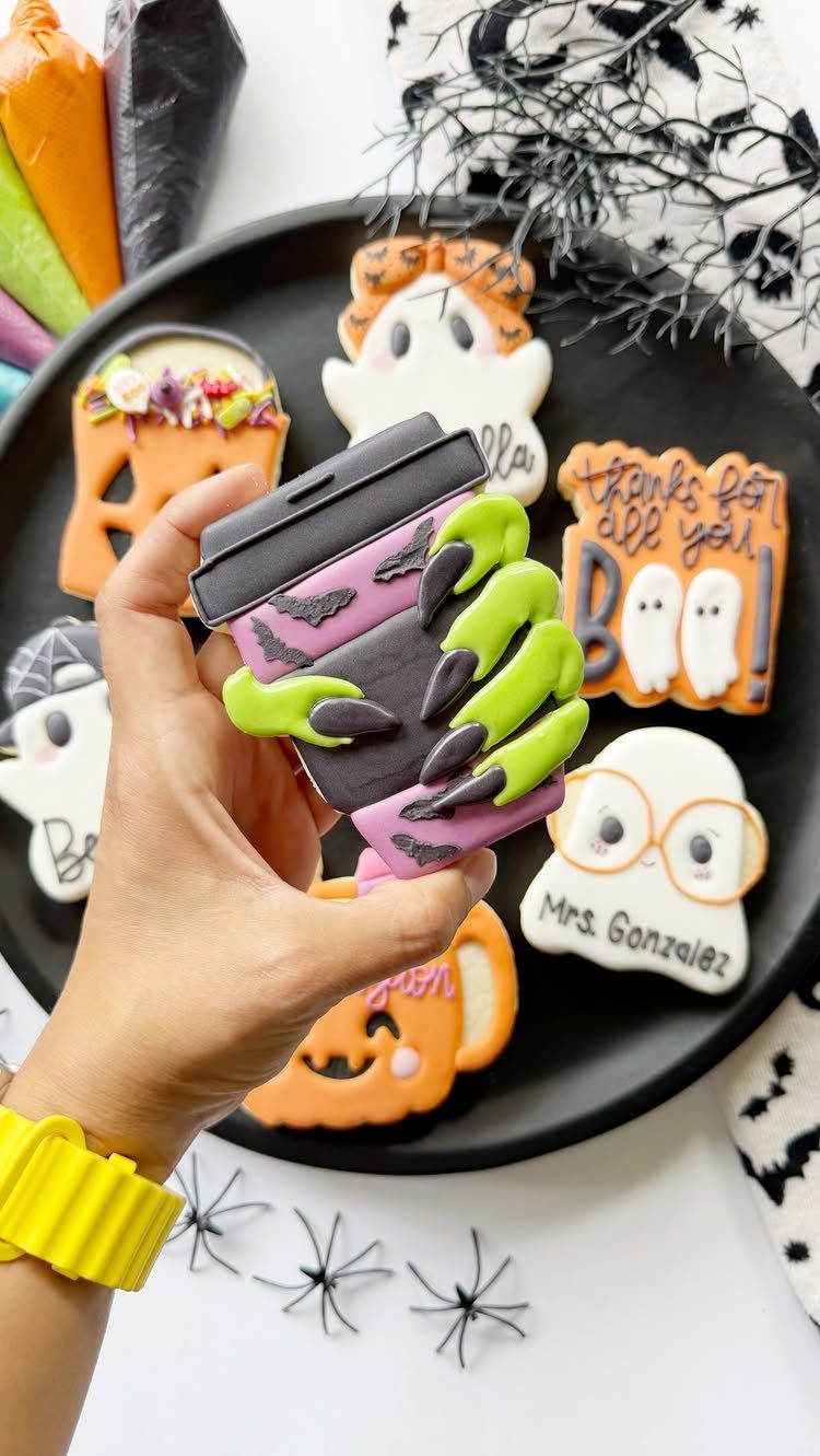 11 Gifts for Halloween Lovers: Candles, Socks and More 4 Decorated Halloween cookies on a black plate, including a purple coffee cup and ghosts.